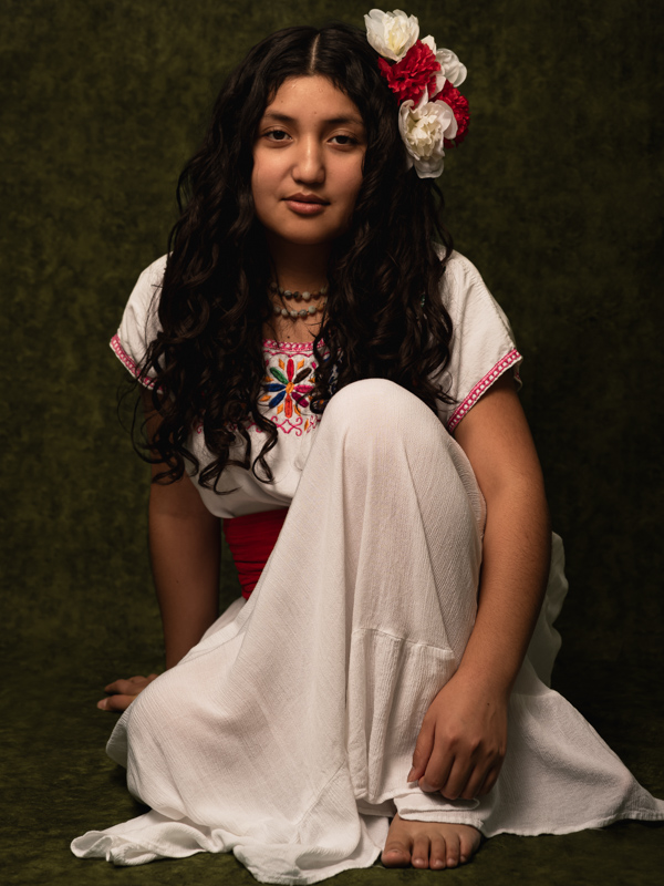 color; Beautiful young girl wearing white dress, with white and red roses on her long curly hair. Background is green and moody. 